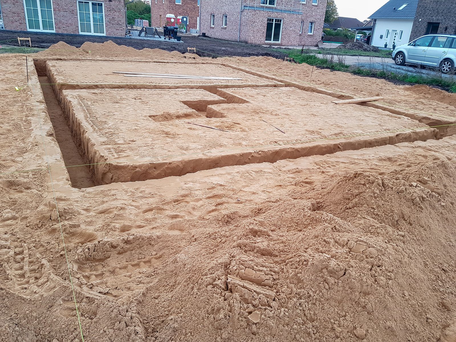 Foundation excavation for a building, rectangular with a central cutout, dirt piles surrounding.