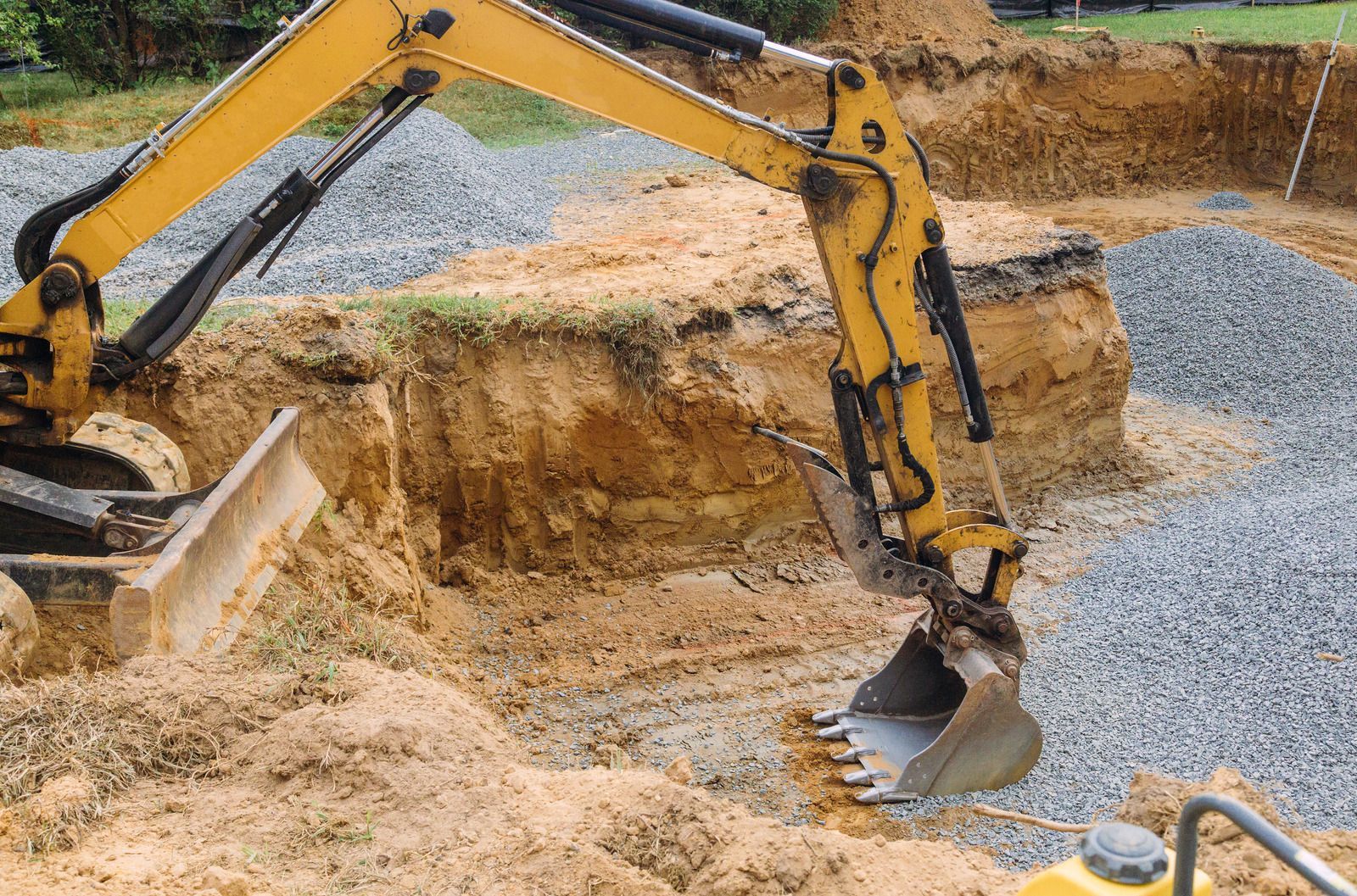 Yellow excavator digging in a construction site with gravel base.