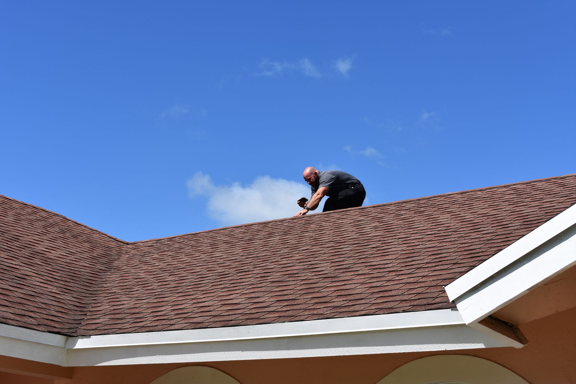 Person on a brown shingled roof under a blue sky, possibly inspecting it.