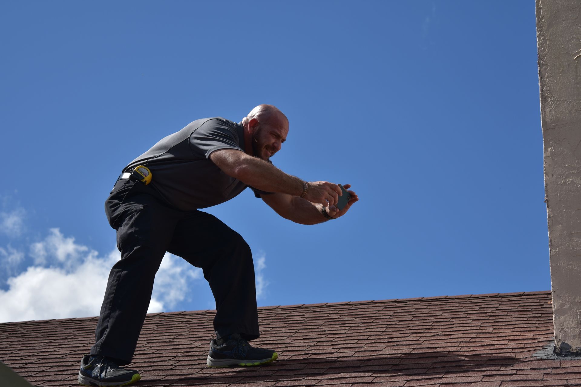 Man on a rooftop, reaching towards something, blue sky in the background.