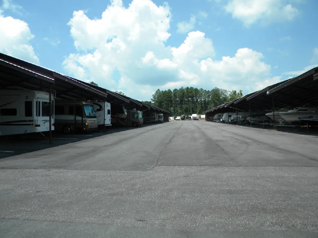 Covered parking area with RVs and boats, under a bright blue sky.