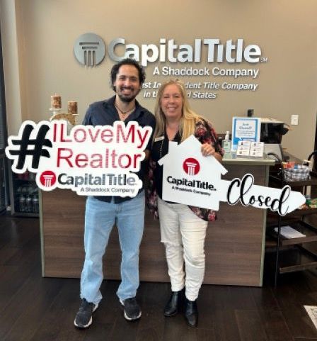 A man and a woman are standing in front of a capital title sign.