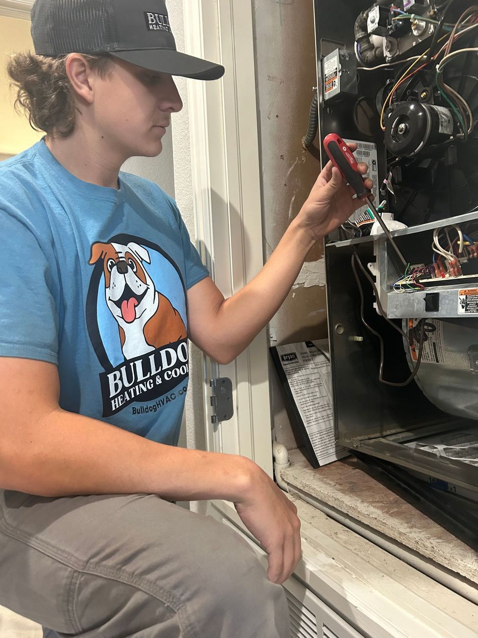 Person in a Bulldog Heating shirt repairs HVAC unit with a screwdriver.