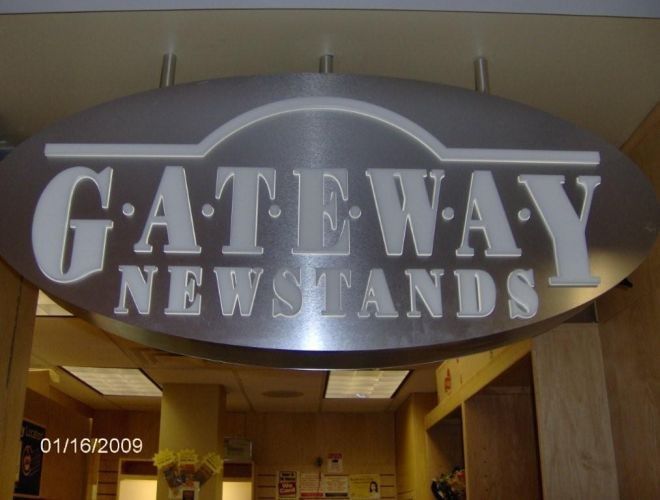 Sign for Gateway Newstands, oval shaped, silver metal with white lettering.