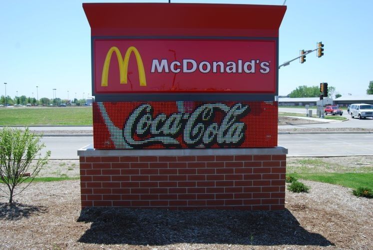McDonald's sign with yellow arches, red background, and Coca-Cola logo on a brick base.