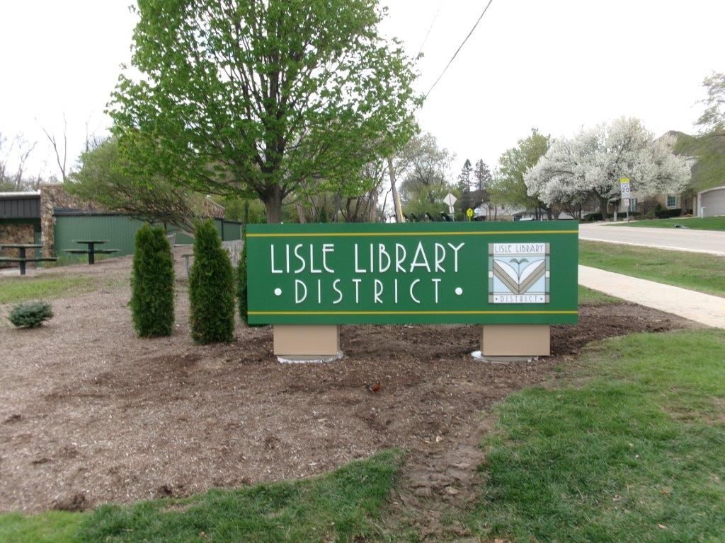 Lisle Library District sign in a grassy area with trees, brown mulch, and a sidewalk.