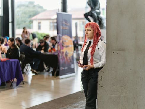 A woman with red hair and a white shirt and tie is standing next to a wall.