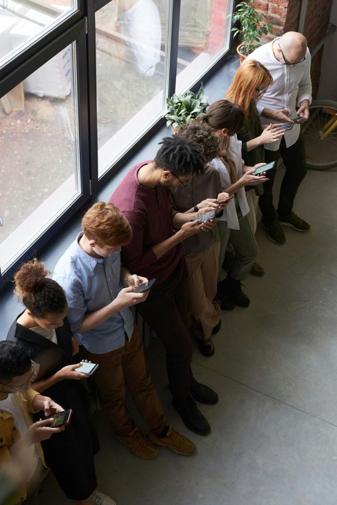 A group of people are standing in front of a window looking at their phones.