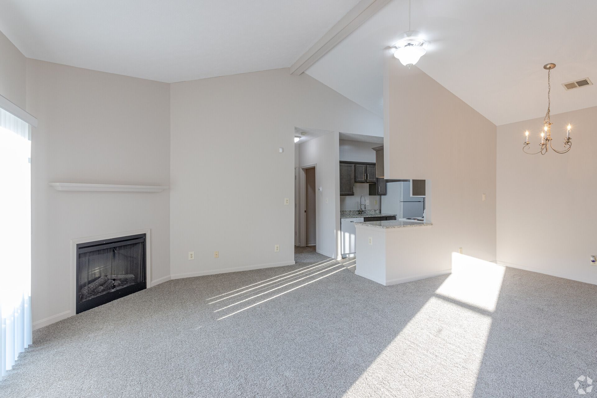 An empty living room with a fireplace and a chandelier.