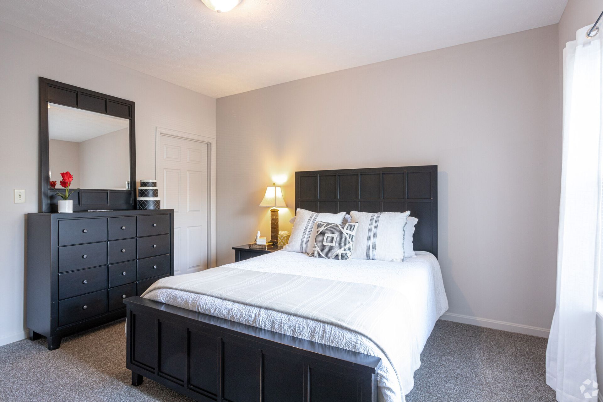 A bedroom with a bed , dresser , mirror and window.