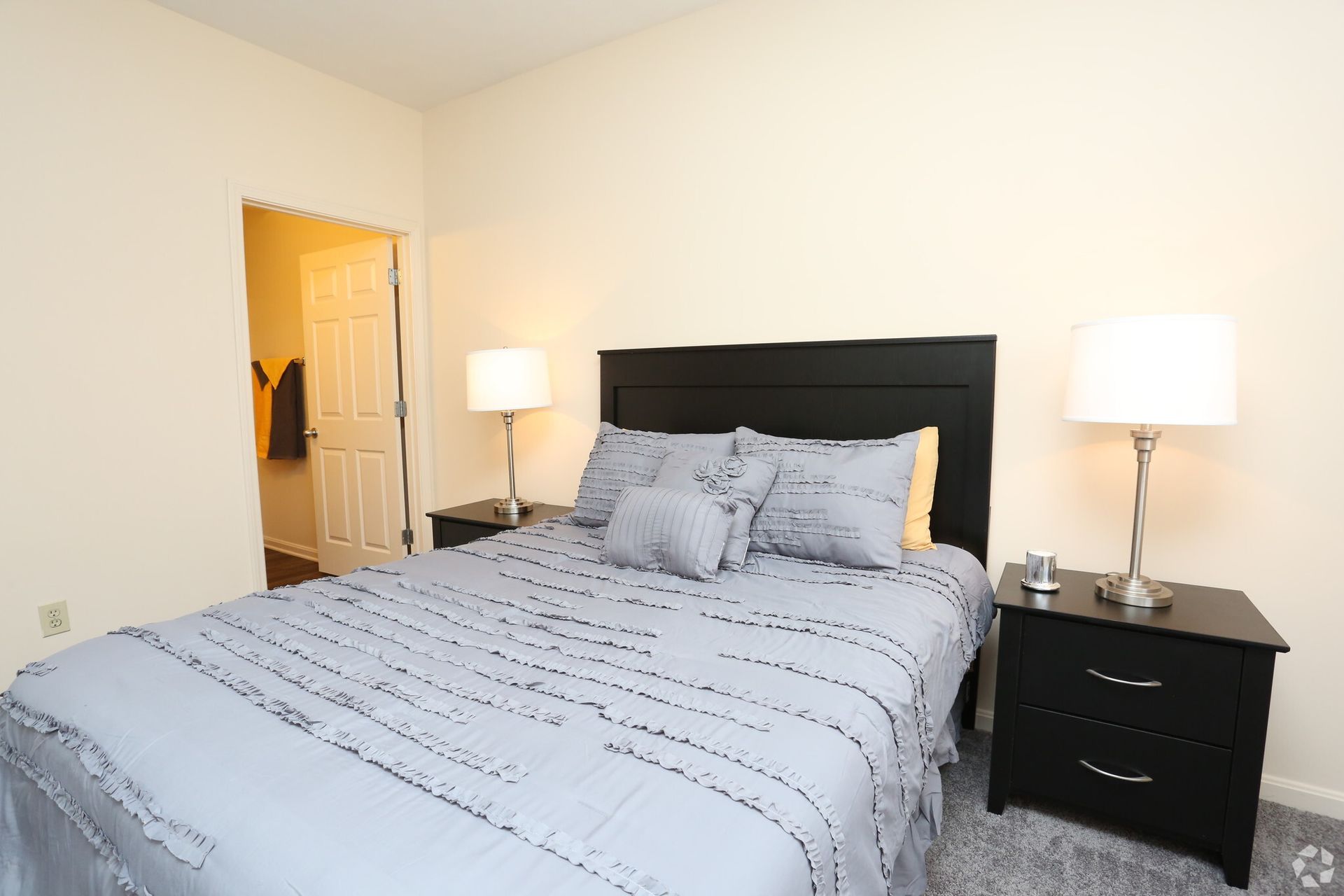 A bedroom with a bed , nightstand , lamps and a door.