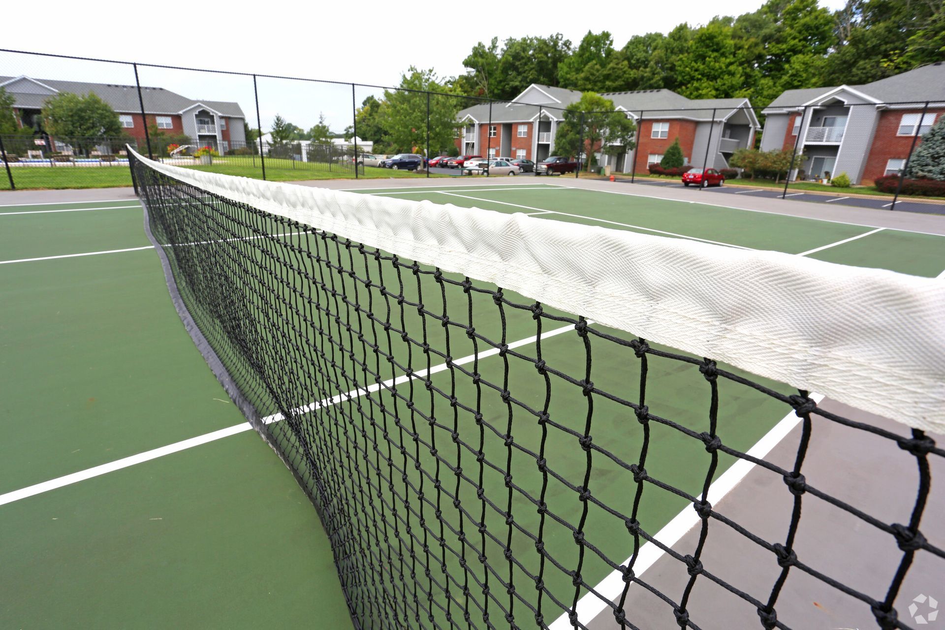 A tennis court with a net in the foreground and buildings in the background