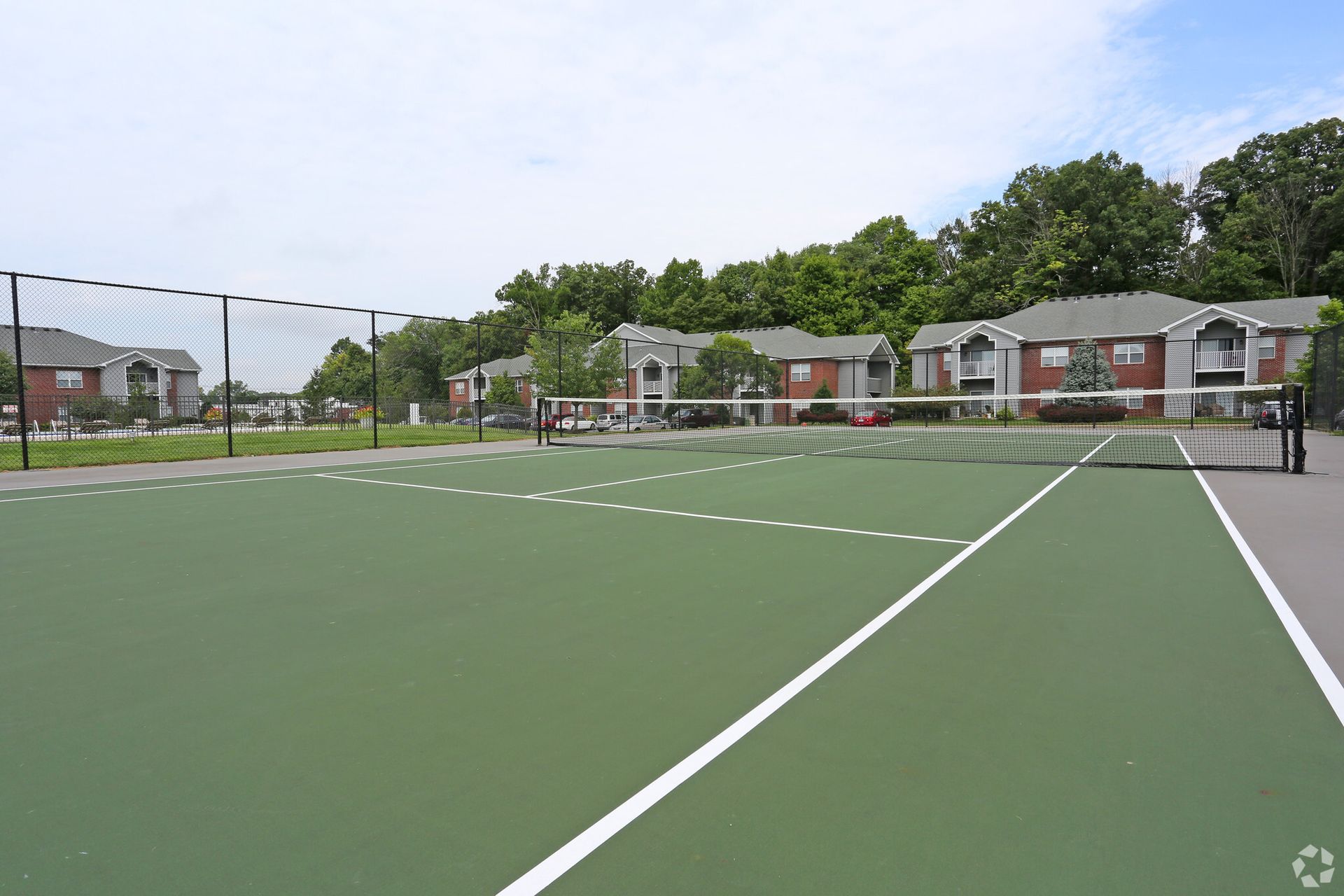 A tennis court with a fence and buildings in the background.