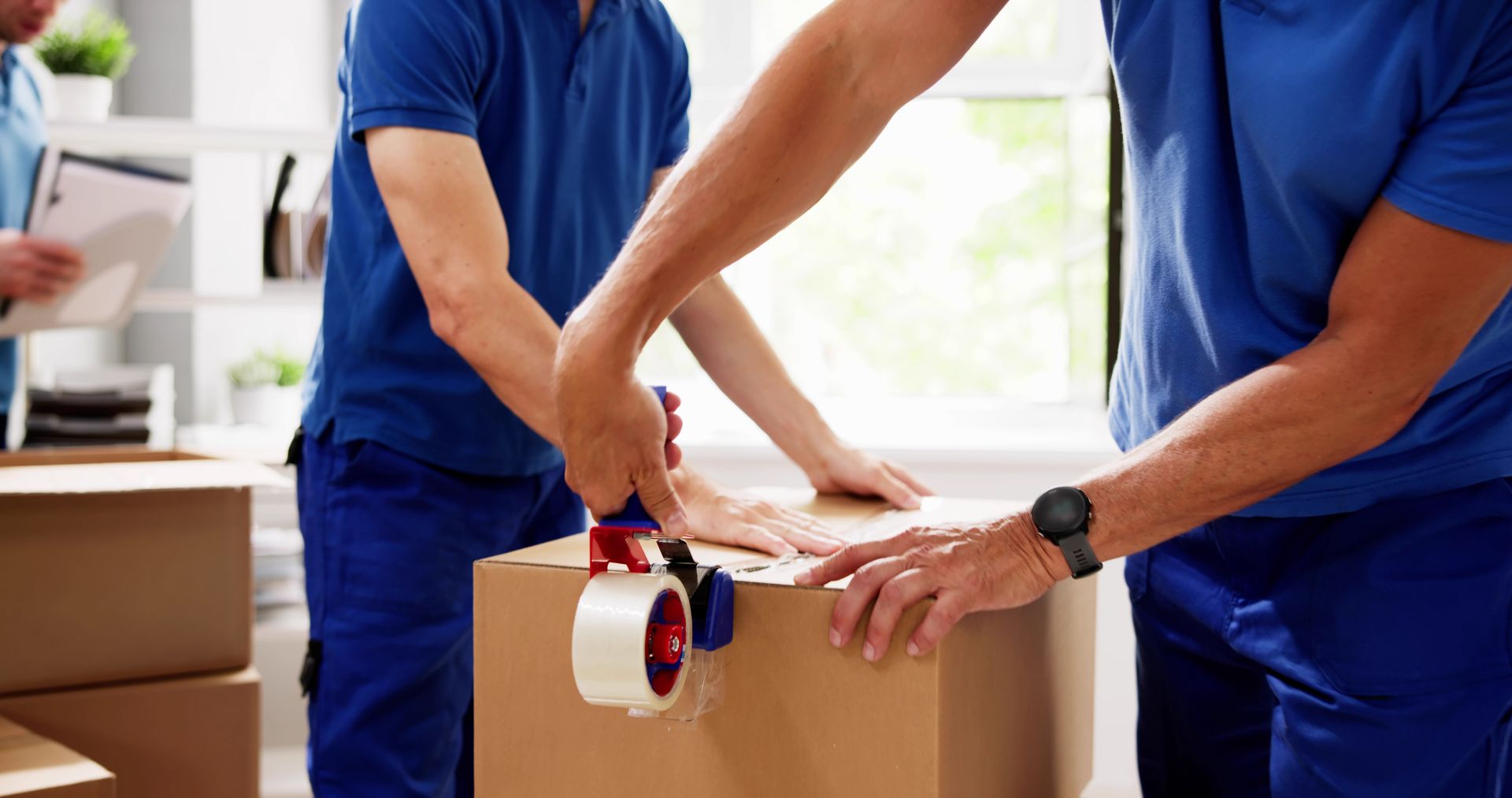 Two men are packing a cardboard box with tape.