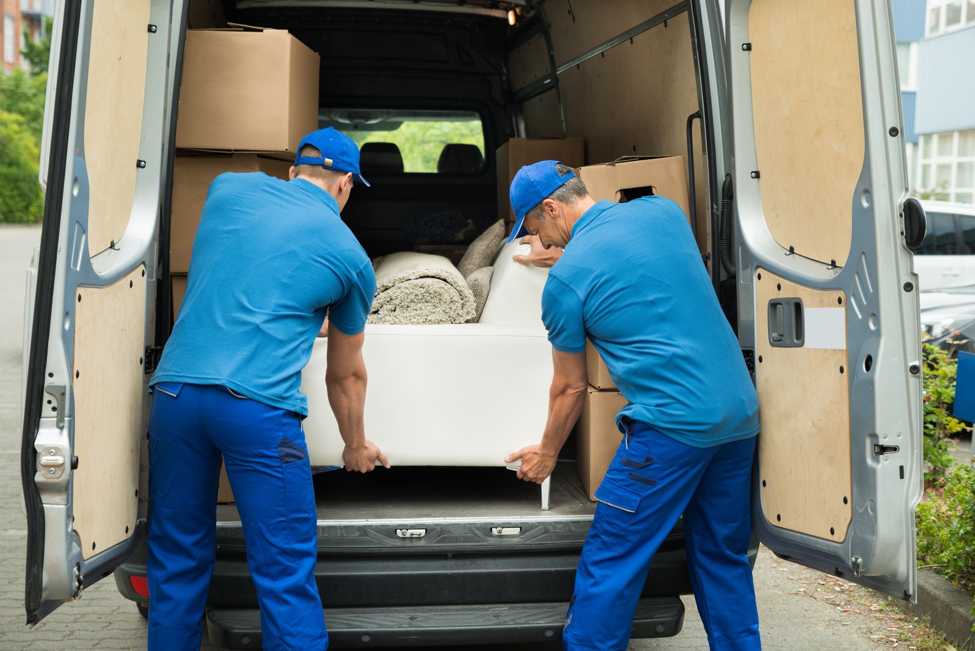 Two men are loading a couch into the back of a van.