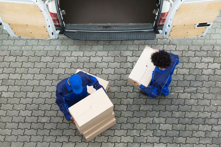Two delivery men are carrying boxes out of a van.