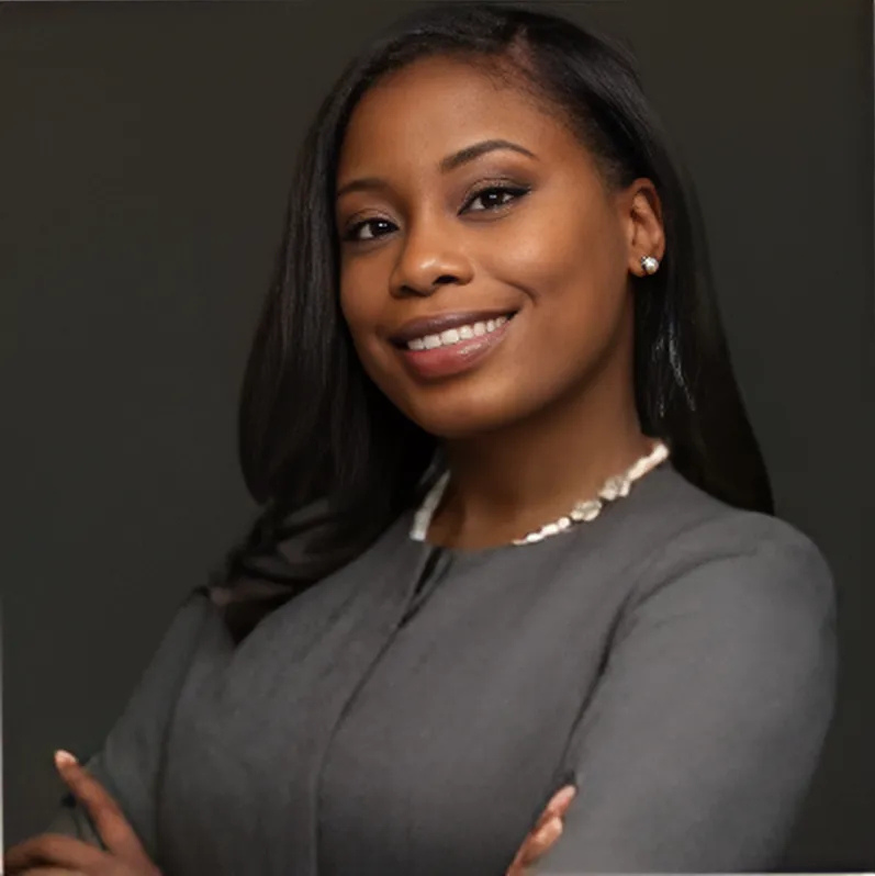 Woman with dark hair in gray blazer smiling, arms crossed.