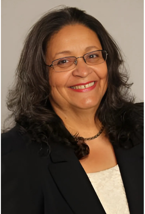 Smiling woman with glasses, dark hair, and dark blazer.