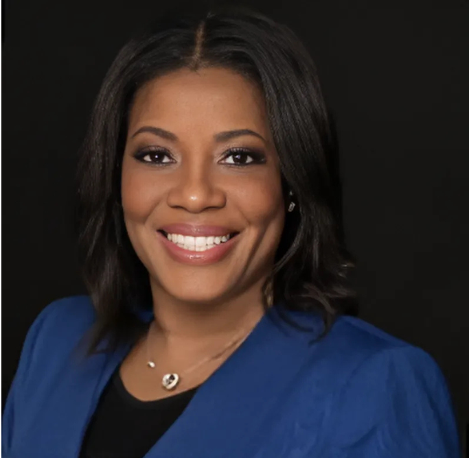 Smiling woman with dark hair in a blue blazer against a black background.