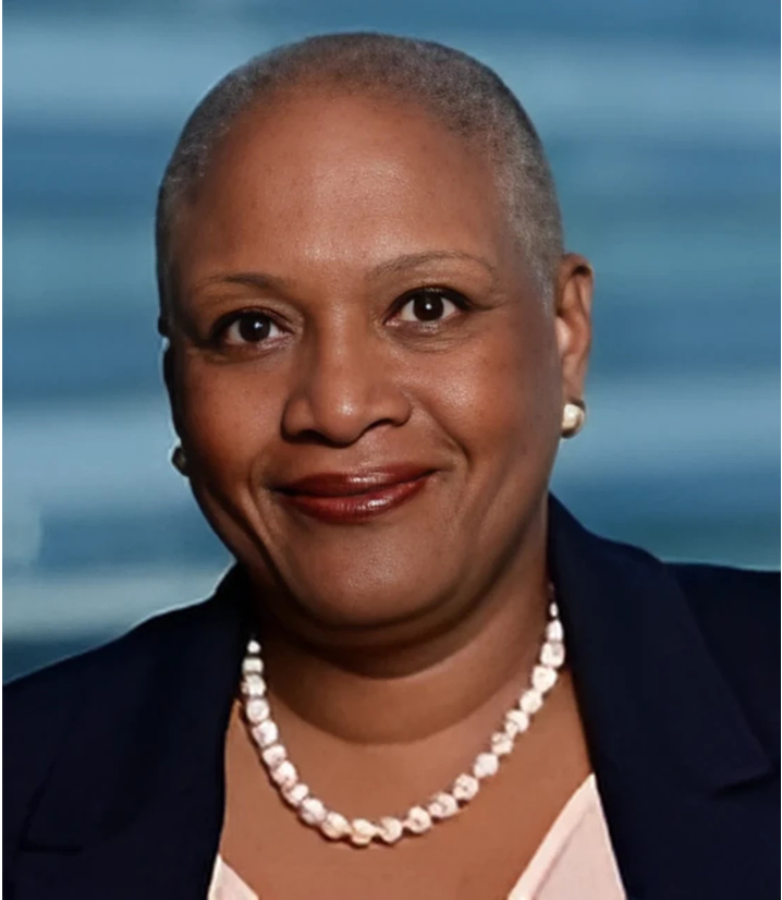 Smiling Black woman with short hair wearing a pearl necklace and navy blazer.