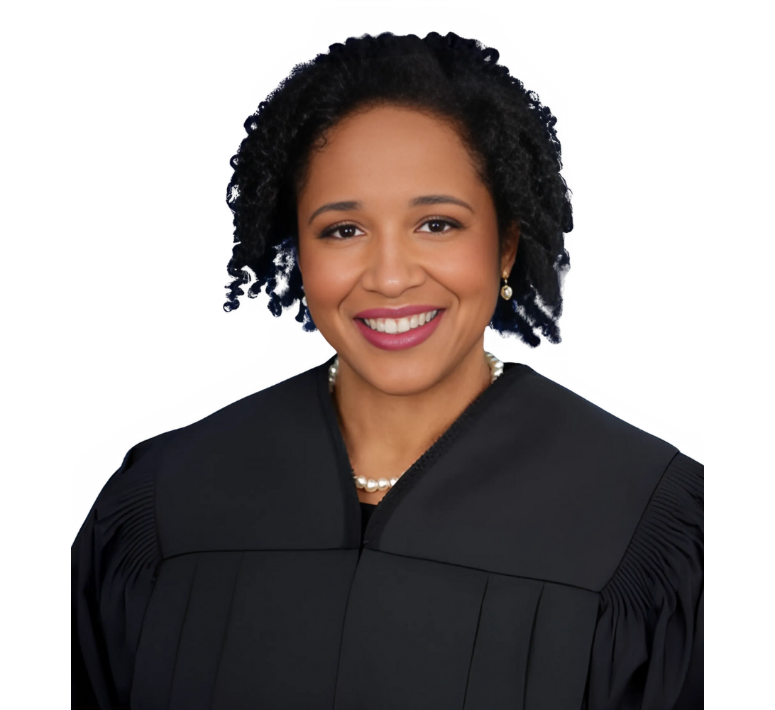 Smiling Black woman judge wearing a black robe, pearl necklace, and dark curly hair.