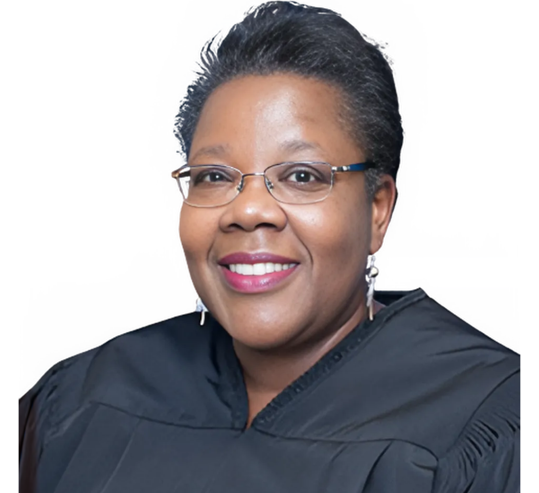 Judge with glasses, smiling, wearing a black robe.