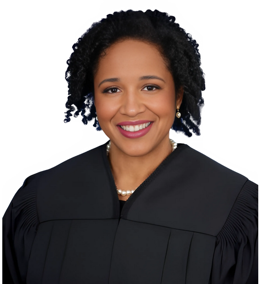 Judge in black robe smiles, wearing pearl necklace.