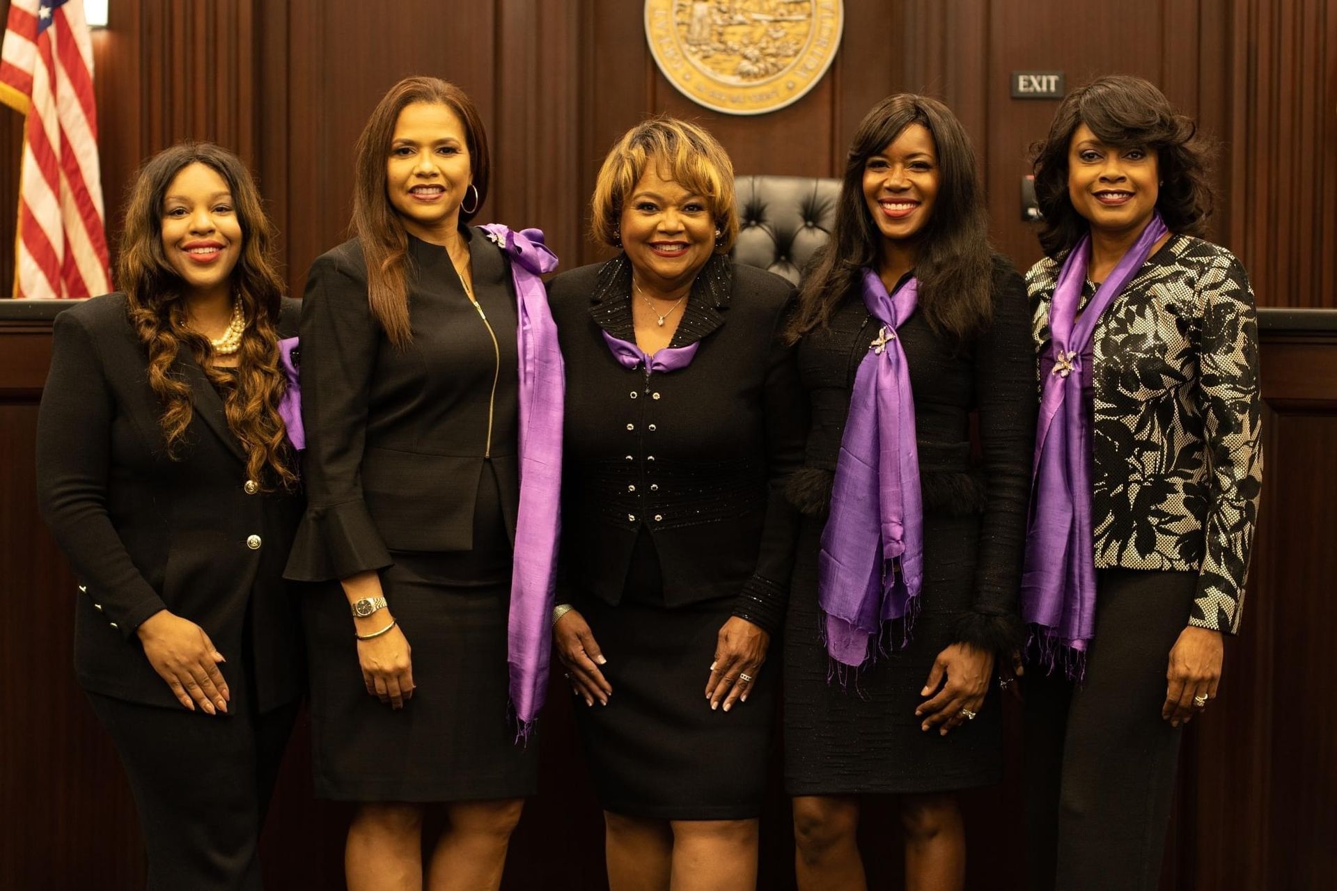 Five Black women in courtroom; wearing black suits and purple scarves; smiles.