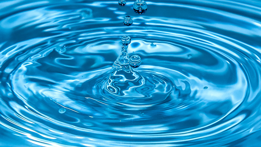 A close-up of water droplets creating ripples on a blue surface.