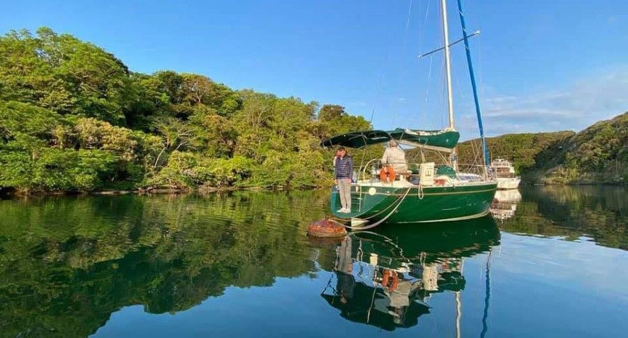 A green sailboat is docked in the middle of a cove.