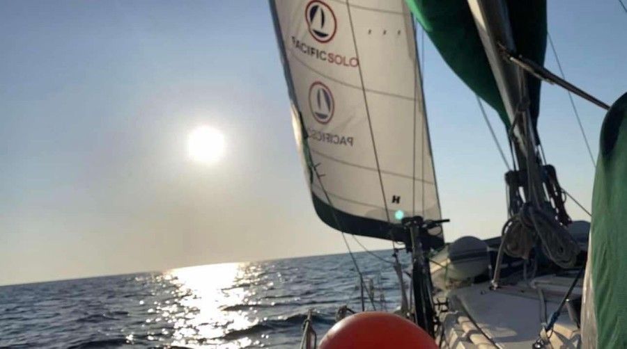 A sailboat in the ocean with the sun shining through the sails