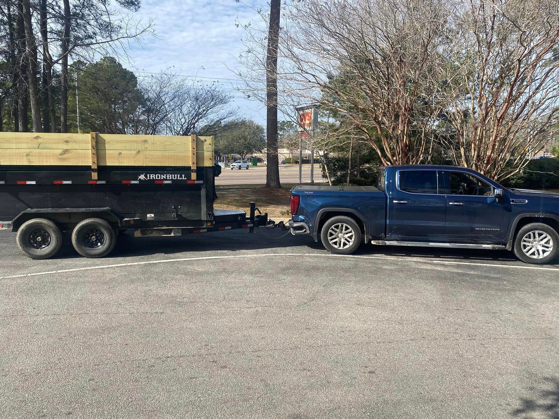 A blue truck is towing a dump trailer in a parking lot. | Summerville, SC | Trash Masters