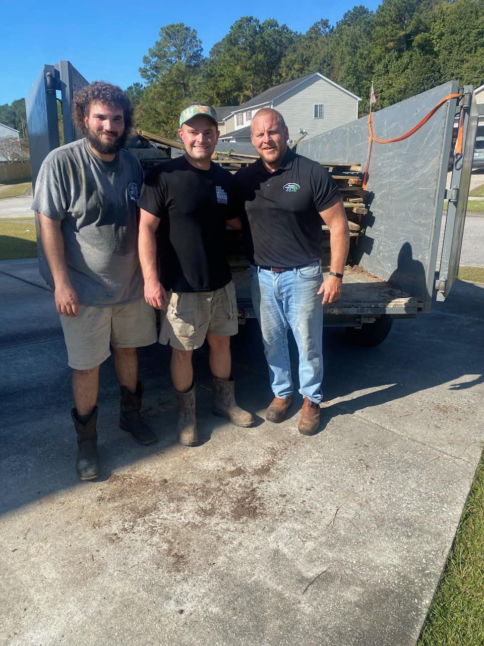 Three men are posing for a picture in front of a trailer. | Summerville, SC | Trash Masters