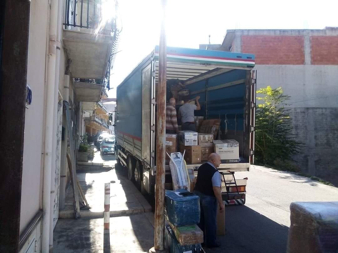 Un camion parcheggiato in una strada stretta viene caricato con delle scatole da due persone.