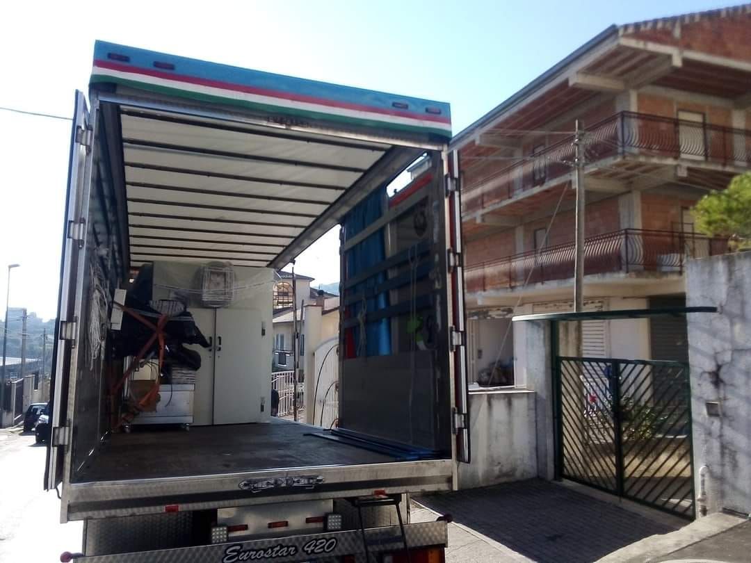 Camion aperto con rampa, parcheggiato vicino a un edificio. I portelloni posteriori sono aperti, rivelando il contenuto all'interno.