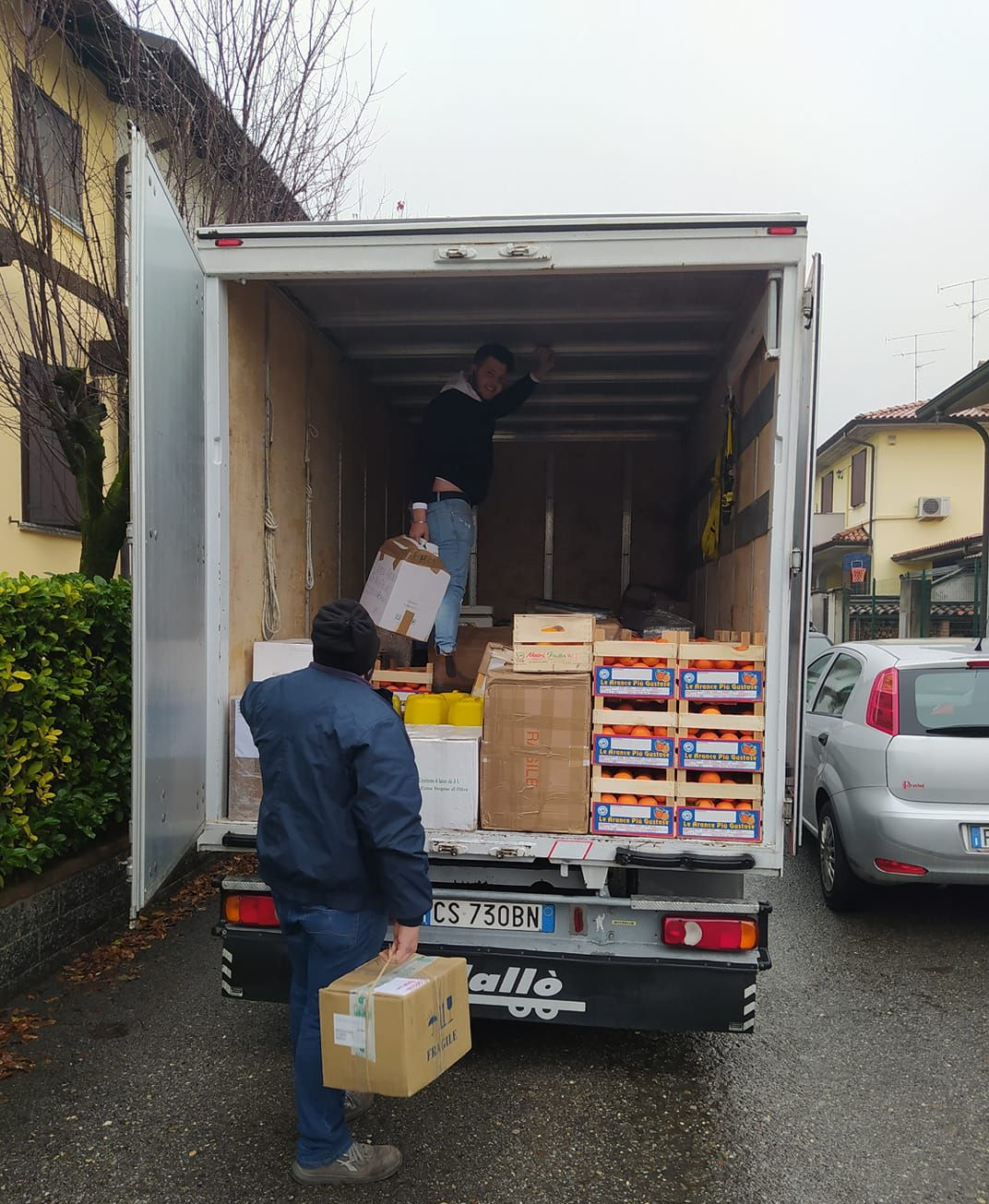 Due persone caricano scatole di cibo su un camion per le consegne, all'aperto.