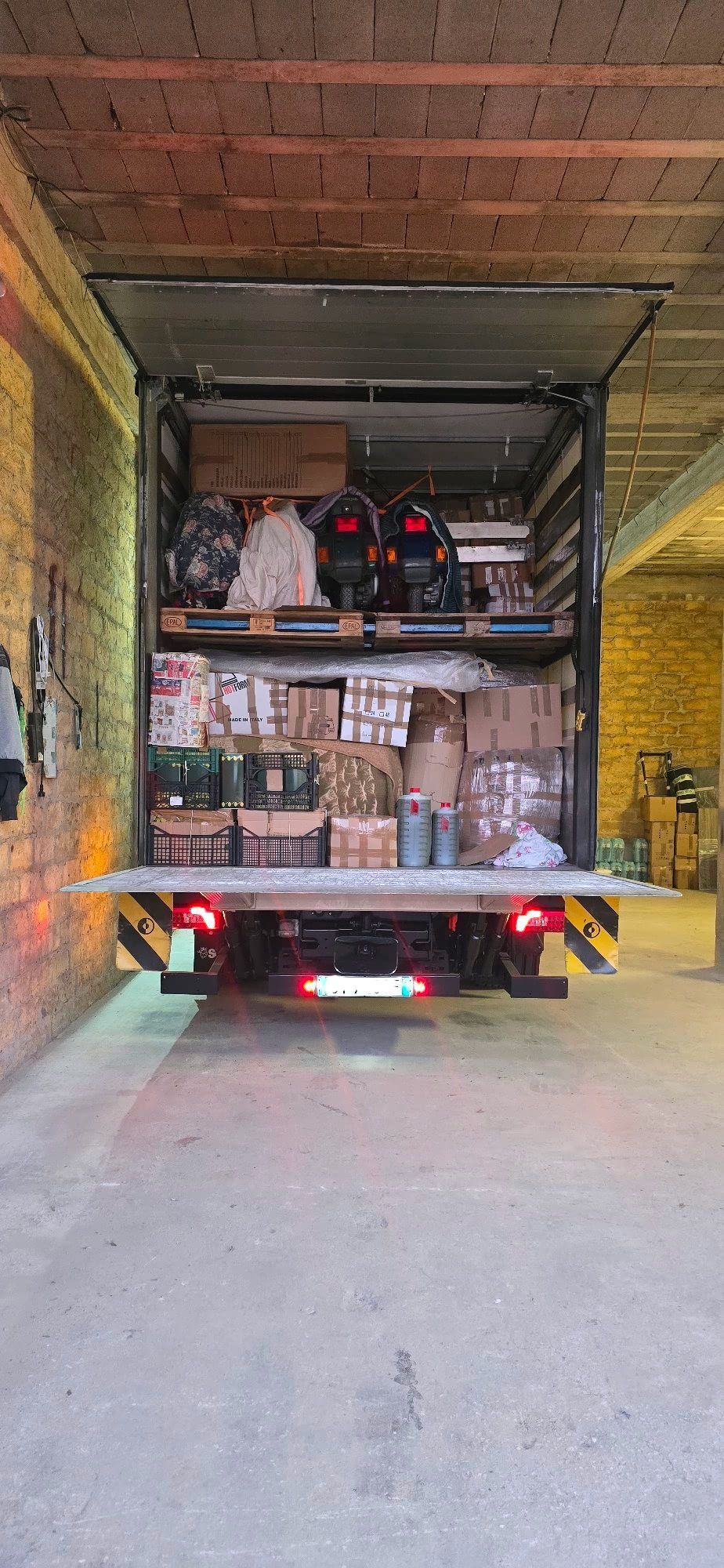 Retro di un camion carico di scatole, attrezzi e forniture, aperto in un magazzino.