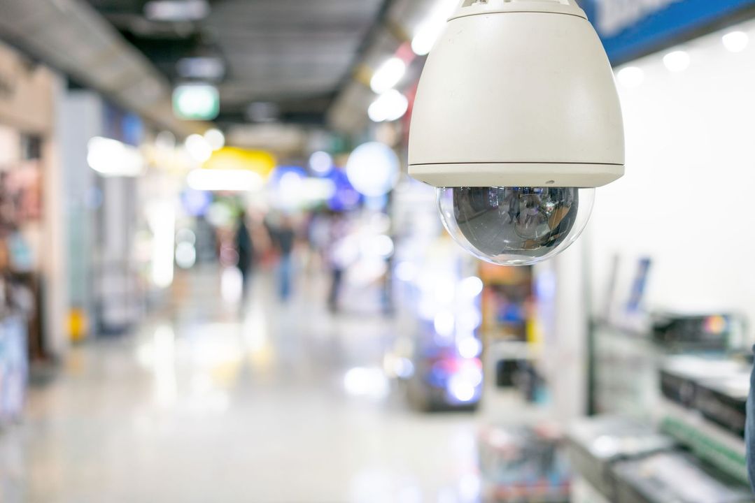 Telecamera di sicurezza installata in un centro commerciale, che riprende il corridoio affollato con figure sfocate.