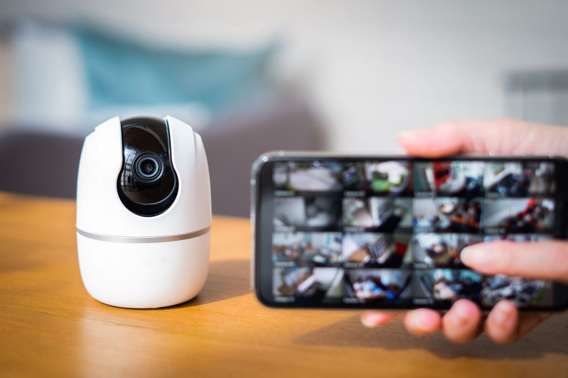 Telecamera di sicurezza bianca e telefono che mostra più riprese.