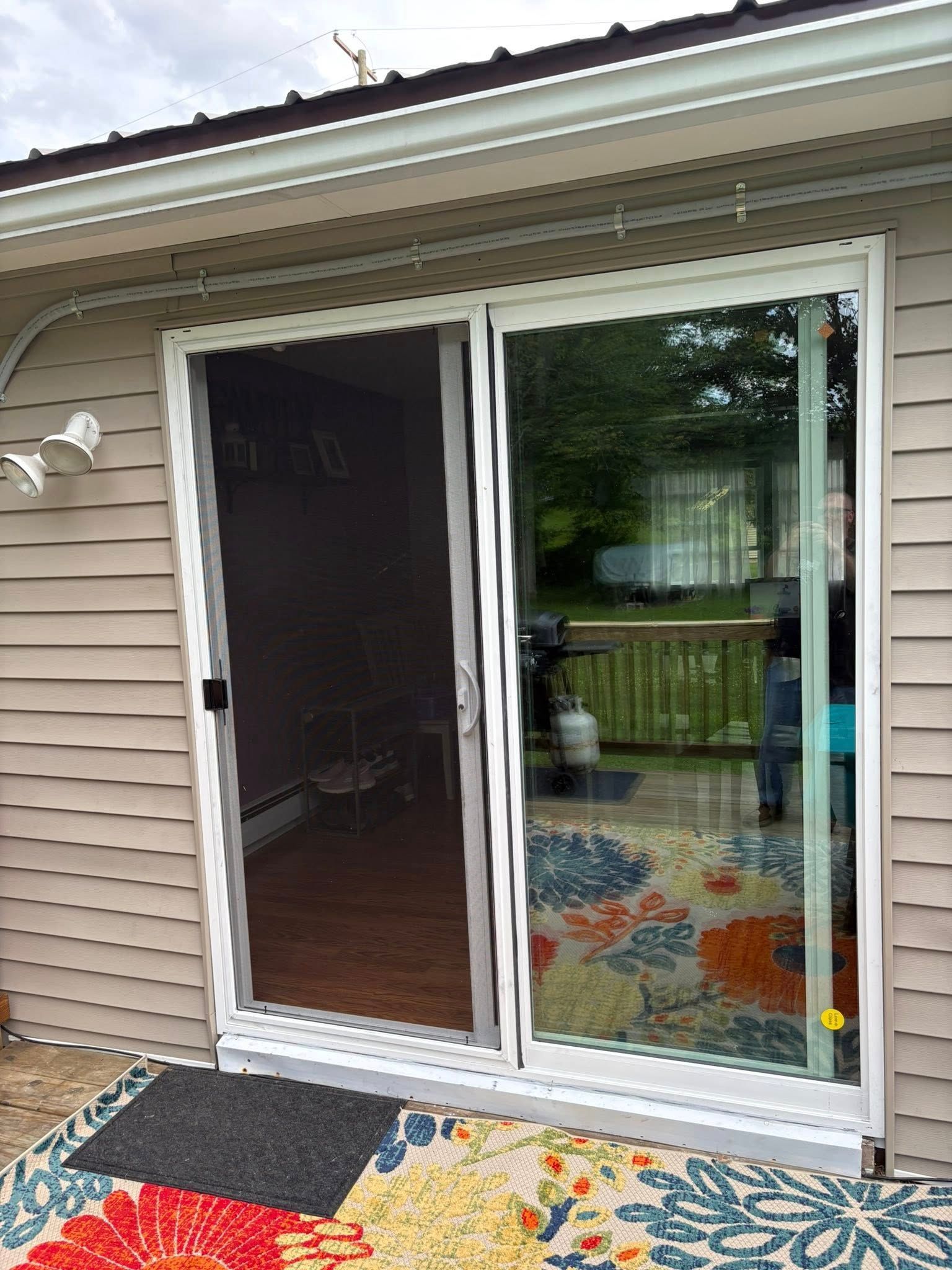 Sliding glass door with a screen door and white frame, on a patio with a colorful rug.