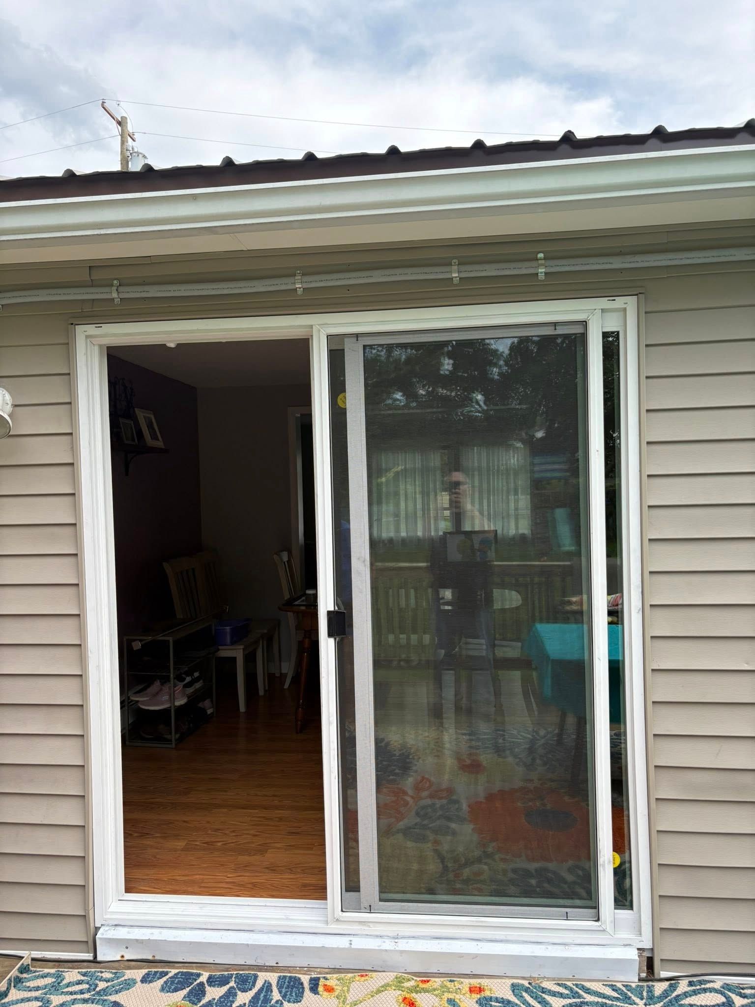 Sliding glass door with white frame and screen. Beige siding and brown roof overhead.