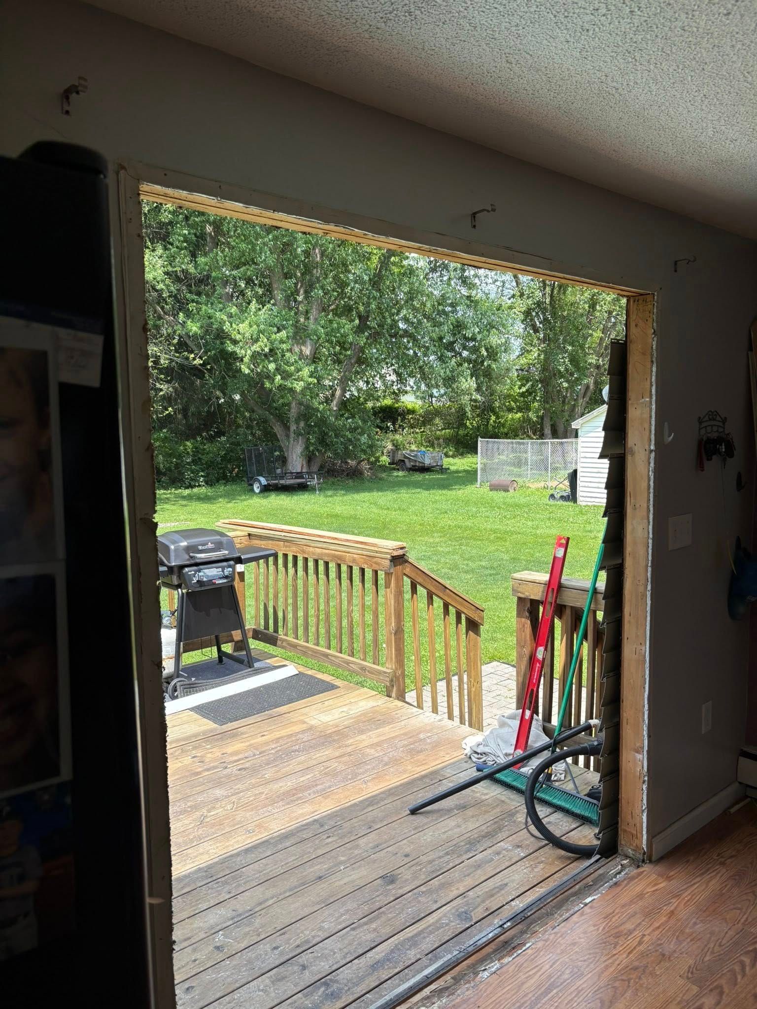 View of a backyard from an open doorway. Includes a wooden deck, a grassy lawn, and a barbecue grill.