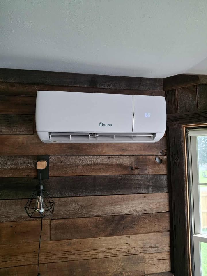 White wall-mounted air conditioner on a rustic wood-paneled wall next to a window and hanging light.