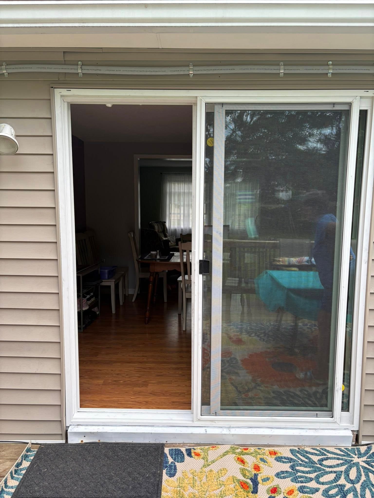 Sliding glass door, one side open, revealing interior. Beige siding, welcome mat, sunlight.