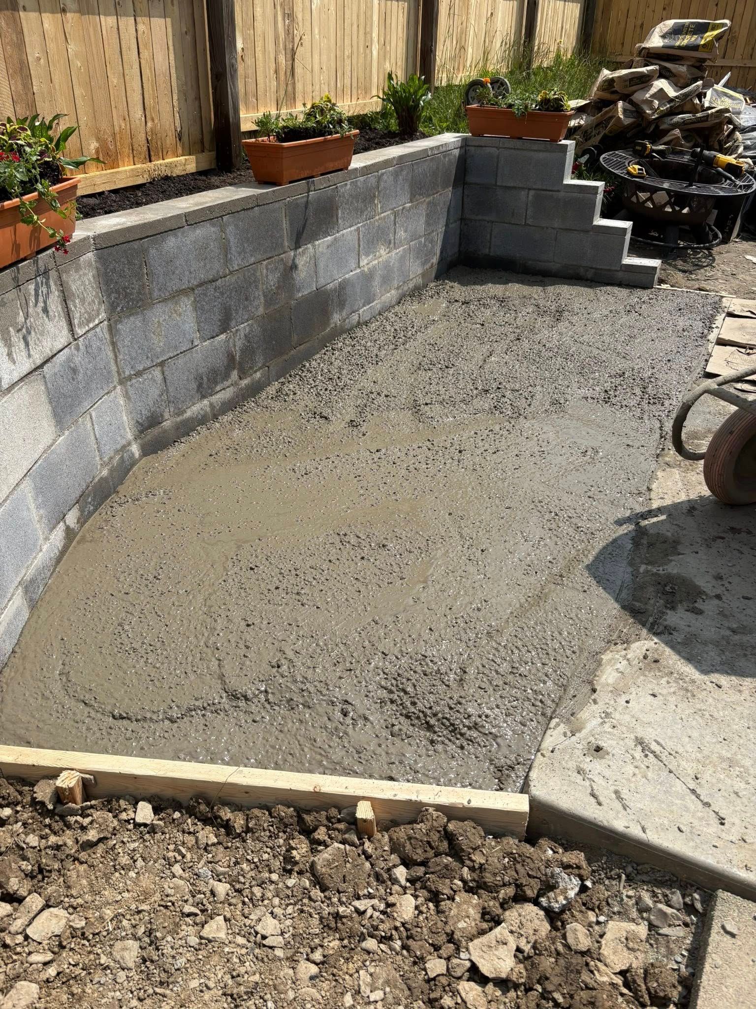Freshly poured concrete patio surrounded by concrete block walls and wooden border.