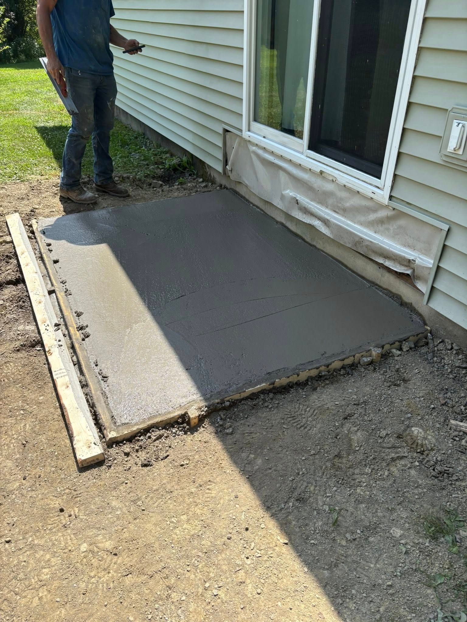 Freshly poured concrete slab by a sliding glass door. A person is standing nearby.