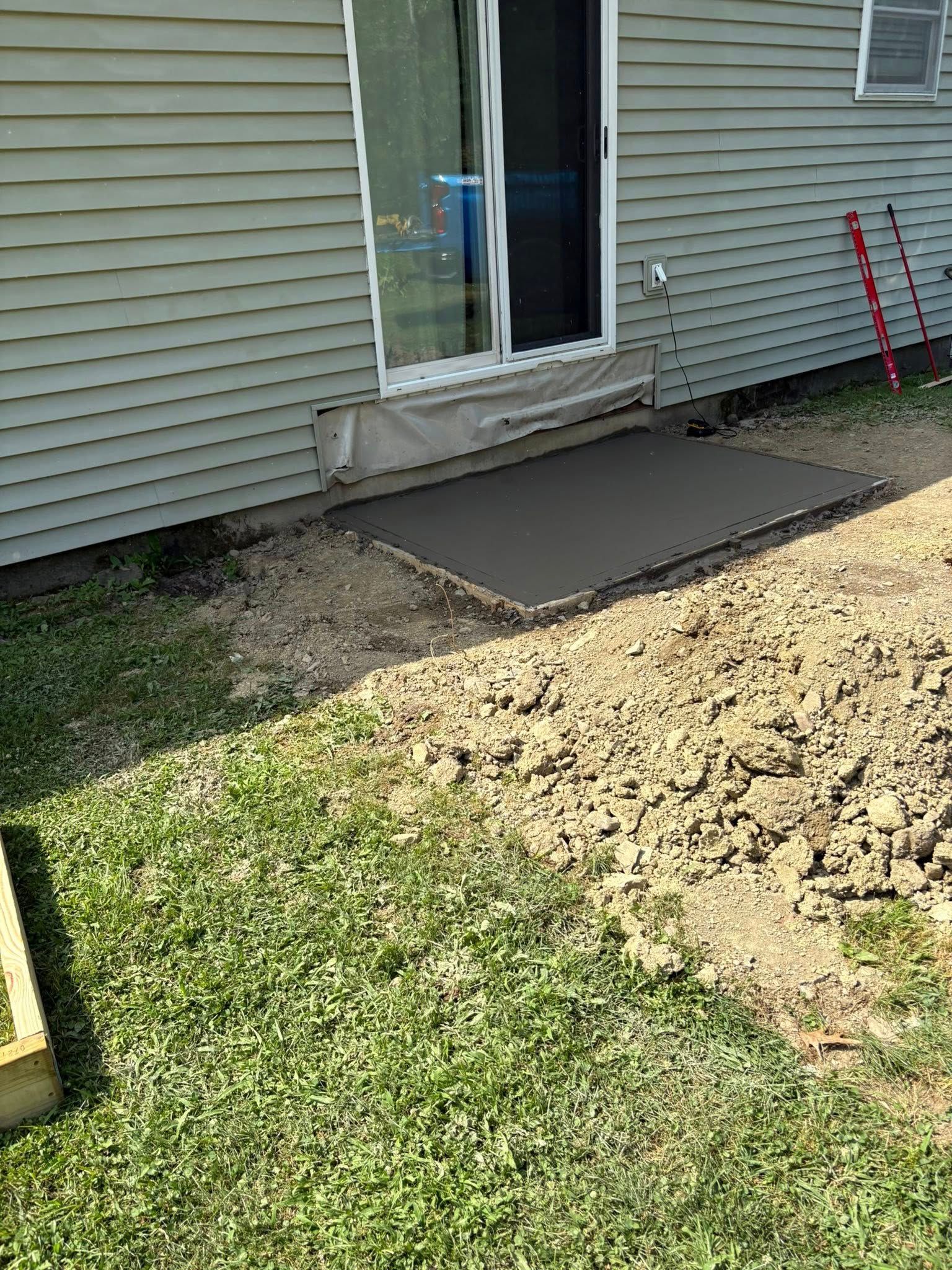A newly poured concrete slab outside a sliding glass door, surrounded by dirt and grass.
