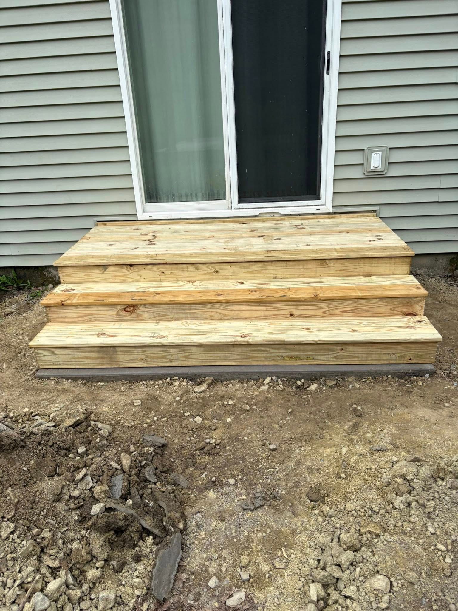 Wooden outdoor steps in front of a sliding glass door, set on a gravel base.