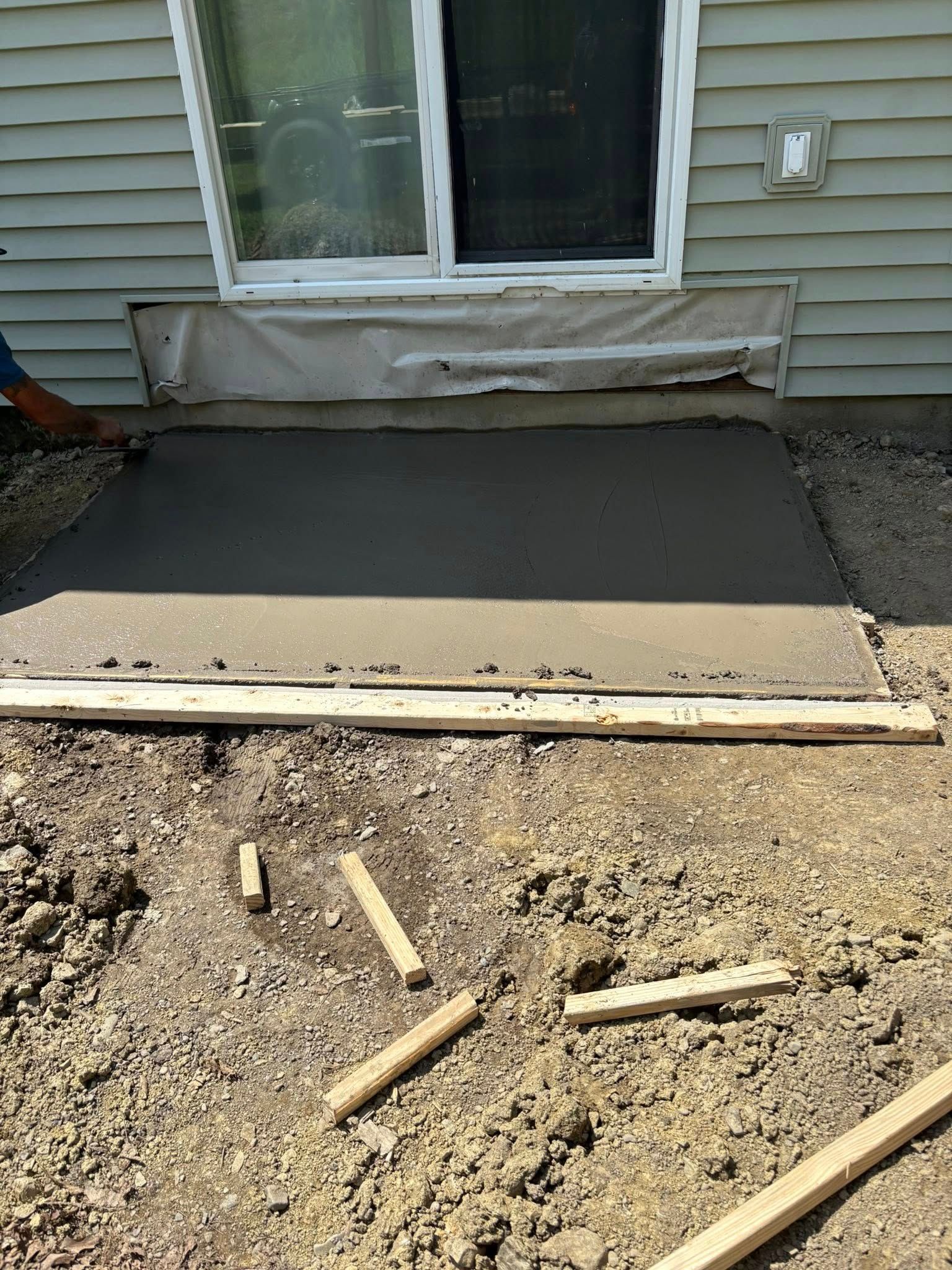 Freshly poured concrete slab in front of a sliding glass door, wooden frame visible.