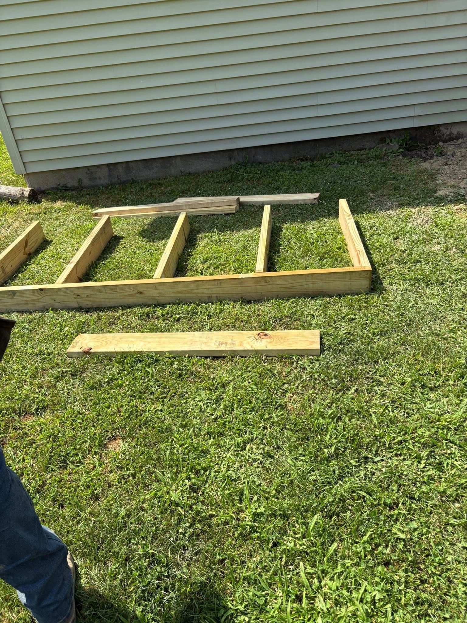 Wooden frame construction on green grass near a house with white siding.